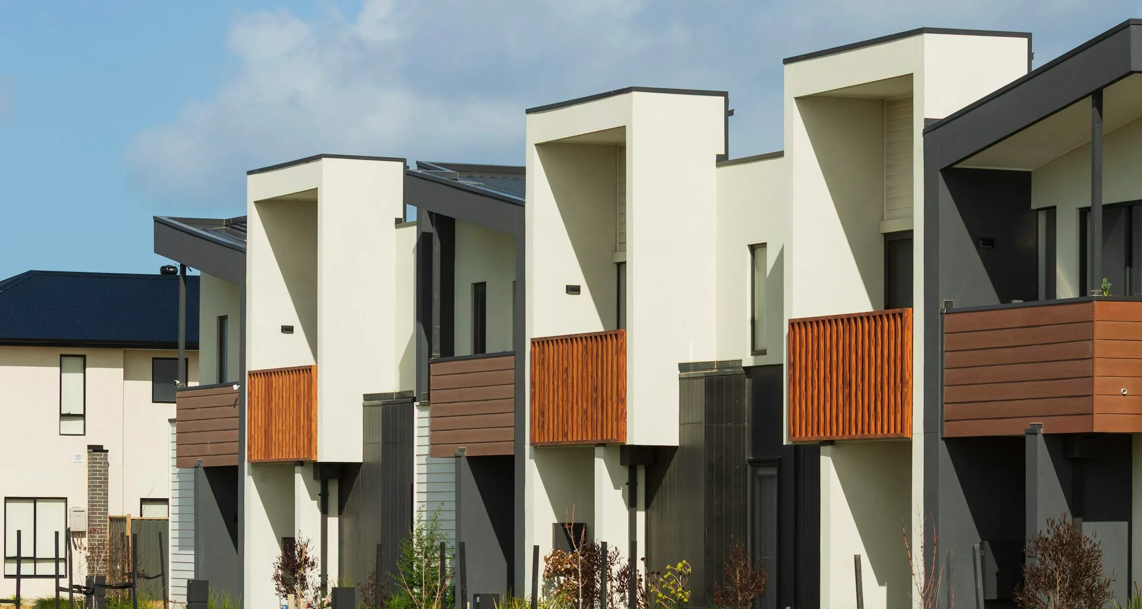 Modern Australian townhouses with smooth white facades, grey cladding panels and timber balconies